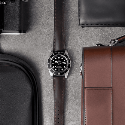 Watch with brown strap on a textured surface with bags and a wallet